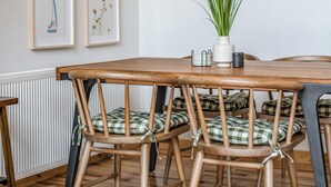 Un comedor con mesa y sillas de madera, una obra de arte enmarcada en la pared y una planta en maceta.