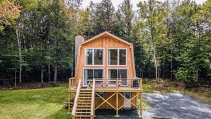 Una cabaña de madera con un balcón y una escalera, rodeada de un bosque.