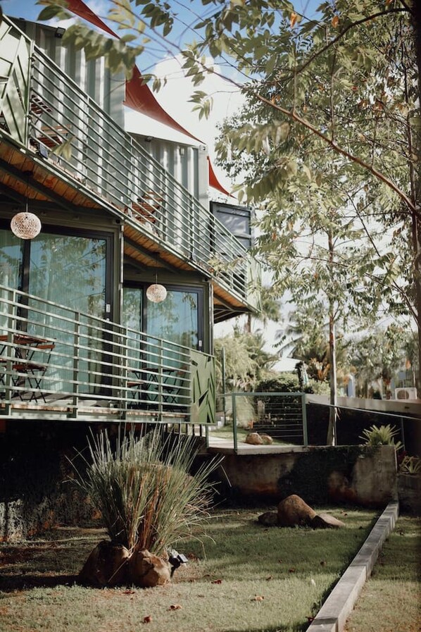 A modern building with a balcony, large windows, and a well-maintained garden with rocks and plants.