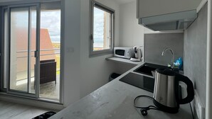 A modern kitchen with a large window, a microwave, a kettle, and a sink. - Nice T2 with 2 balconies on the seafront (Ouistreham)