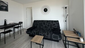 A modern living room with a black and white patterned sofa, a wooden coffee table, a black dining table with chairs, and a floor lamp. - Nice T2 with 2 balconies on the seafront (Ouistreham)
