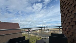 A balcony with wicker furniture, a metal railing, and a view of the beach and distant buildings. - Nice T2 with 2 balconies on the seafront (Ouistreham)