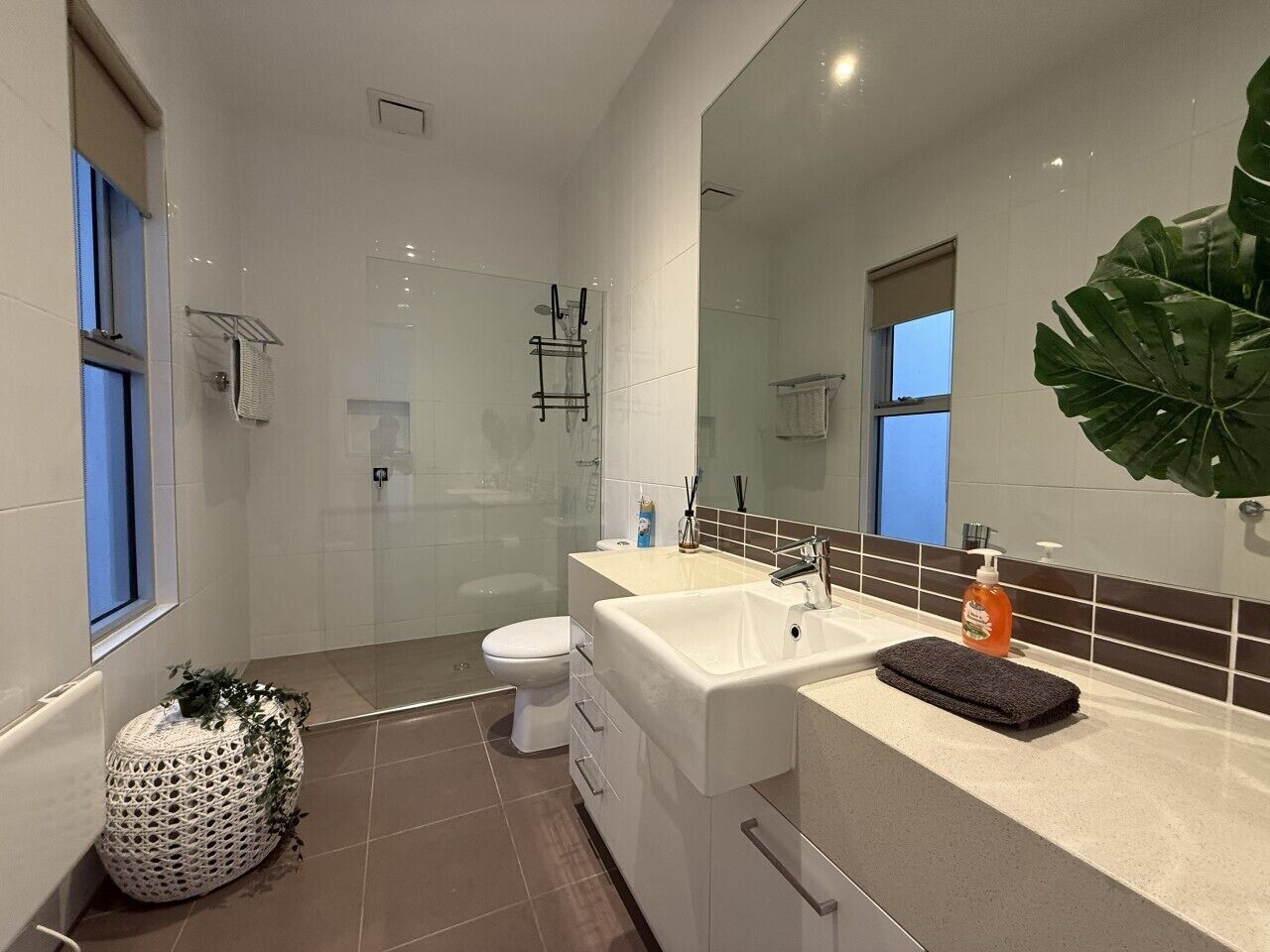 Ein modernes Badezimmer mit einer Duschkabine aus Glas, einer weißen Toilette, einem beige farbenen Waschbecken mit schwarzem Handtuch und einem großen Spiegel.
