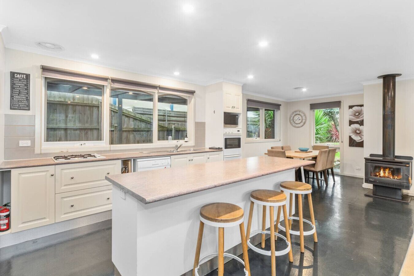 A modern kitchen with a large island, bar stools, a built-in stove, and a dining area with a view of greenery.