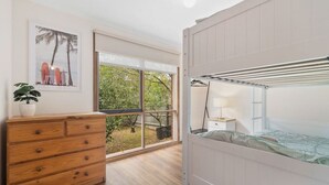 Un dormitorio con una cama litera, un aparador de madera, una ventana con vista a árboles y un cuadro en la pared.