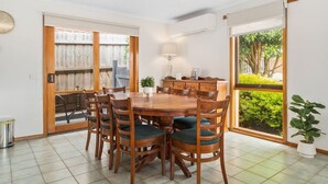 Un comedor con una mesa y sillas de madera, una planta en maceta y vistas a zonas verdes a través de una puerta corredera.