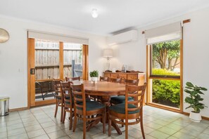 Enjoy meals in this cozy dining area with a round table and six chairs, surrounded by lush views and a small potted plant.