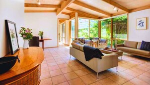 A spacious living area with a wooden ceiling, large windows, a sofa, and a dining table. - Garden Cottage - Somers (Somers)