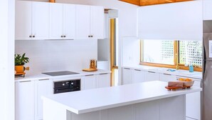 A modern kitchen with white cabinetry, a central island, a built-in oven, and a window with a view. - Garden Cottage - Somers (Somers)