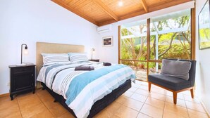 A bedroom with a bed, bedside tables, a chair, and a window with a view of greenery. - Garden Cottage - Somers (Somers)