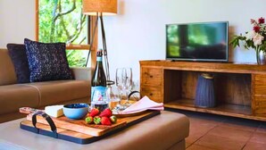 A living room with a sofa, a TV, a wooden cabinet, a tray with strawberries, a bottle, and glasses. - Garden Cottage - Somers (Somers)