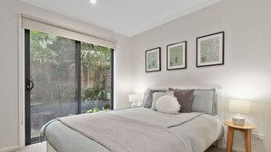 Une chambre avec un grand lit, une porte-fenêtre coulissante donnant sur un balcon et trois tableaux encadrés accrochés au mur.