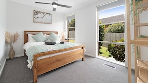A bedroom with a wooden bed, a ceiling fan, a window with a view of the backyard, and a bedside plant shelf. - Fresh Seas - Mornington (Mornington)