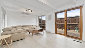 A spacious living room with a large sectional sofa, a coffee table, and a wicker chair. There is a sliding glass door leading to an outdoor area with a wooden fence and bicycles. - Fresh Seas - Mornington (Mornington)