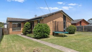 A single-story house with a brick exterior, a front door, and a small front yard with a trampoline and bushes. - Fresh Seas - Mornington (Mornington)