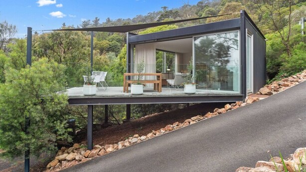 A modern house with a glass extension, outdoor seating, and a view of the surrounding greenery. - Couples Hillside Retreat (McCrae)