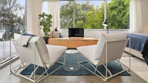 A modern living room with a large window, a flat-screen TV, and two white armchairs. - Couples Hillside Retreat (McCrae)