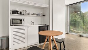 A modern kitchen with white cabinetry, a microwave, a coffee maker, and a dishwasher. There is a round wooden table with a black chair. - Couples Hillside Retreat (McCrae)