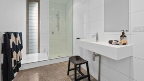 A modern bathroom with a glass-enclosed shower, a white vanity with a mirror, and a stool. - Couples Hillside Retreat (McCrae)