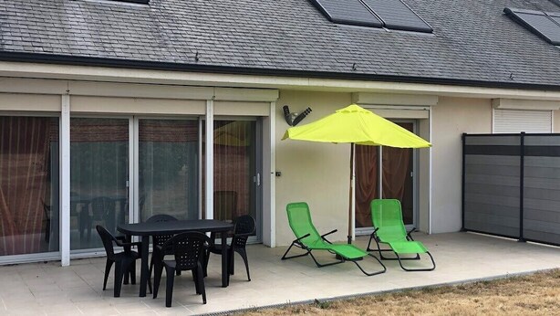 A covered patio with a table and chairs, a yellow umbrella, and green lounge chairs.