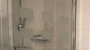 A glass-enclosed shower area with a chrome faucet and a small shelf.
