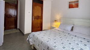 Un dormitorio con una cama, una mesita de noche, un reloj de pared, una puerta y un cuadro en la pared.