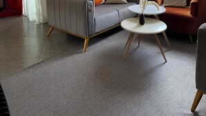 Una sala de estar moderna con un sofá gris, un sillón naranja más pequeño y una mesa redonda de centro con un florero.