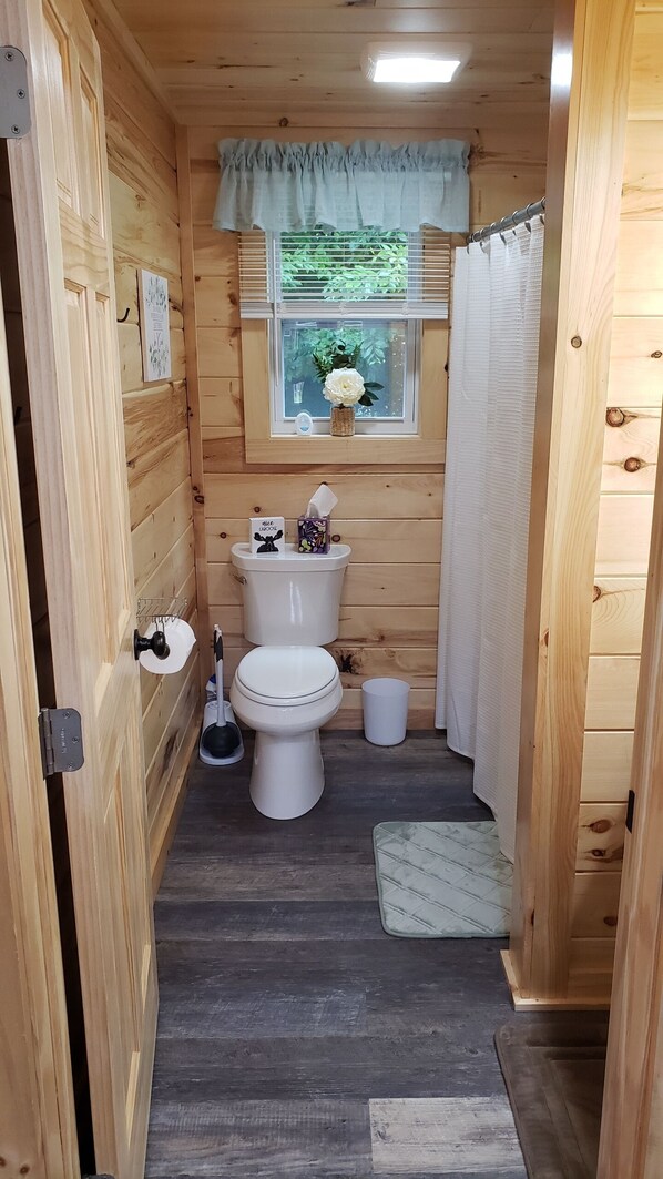 A wooden interior with a toilet, a small window with a curtain, and a wooden door.
