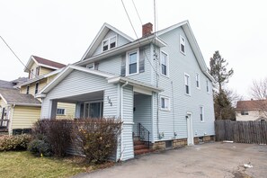 A two-story house with a front porch, a chimney, and a wooden fence.