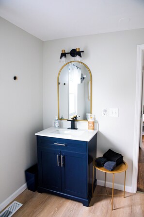 A bathroom with a white sink, dark blue cabinet, gold-framed mirror, and a small round table with towels.