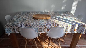 A dining table with a colorful patterned tablecloth, two white chairs, and a wooden serving tray.