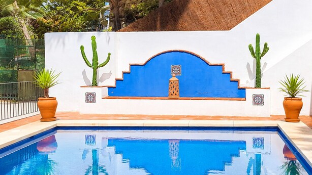 A swimming pool with a blue and white wall, cacti, and terracotta pots.