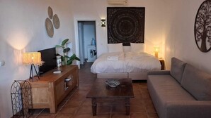 A modern bedroom with a bed, a sofa, a coffee table, and a TV. There is a washing machine in the background.