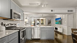 A spacious kitchen with grey cabinets, a large island, stainless steel appliances, and a view of the living area. - Beautiful first-floor 2BR/1.5BA condo near White Rock Lake with resort-style pool, hot tub, cold plunge, dry sauna, and outdoor cardio area—perfect for a relaxing Dallas getaway. (Dallas)