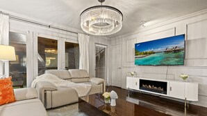 A modern living room with a beige sofa, a glass coffee table, a fireplace, and a large TV mounted on the wall. - Beautiful first-floor 2BR/1.5BA condo near White Rock Lake with resort-style pool, hot tub, cold plunge, dry sauna, and outdoor cardio area—perfect for a relaxing Dallas getaway. (Dallas)