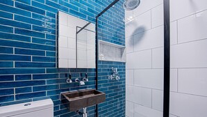 Un baño con paredes de azulejos azules, un inodoro blanco, un lavabo oscuro y una zona de ducha.