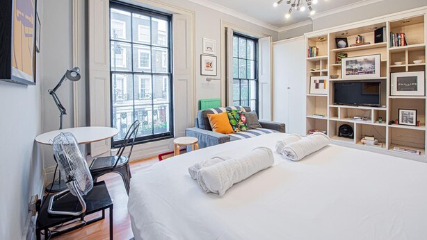 Una habitación de hotel moderna con una cama grande, un escritorio con silla, una estantería y un televisor.