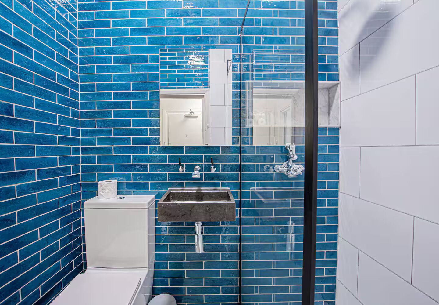 Ein Badezimmer mit blauen Fliesen, einer weißen Toilette, einem Waschbecken mit Marmorplatte und einer Duschkabine aus Glas.