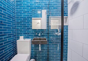 A bathroom with blue-tiled walls, a white toilet, a sink with a marble countertop, and a glass shower enclosure.