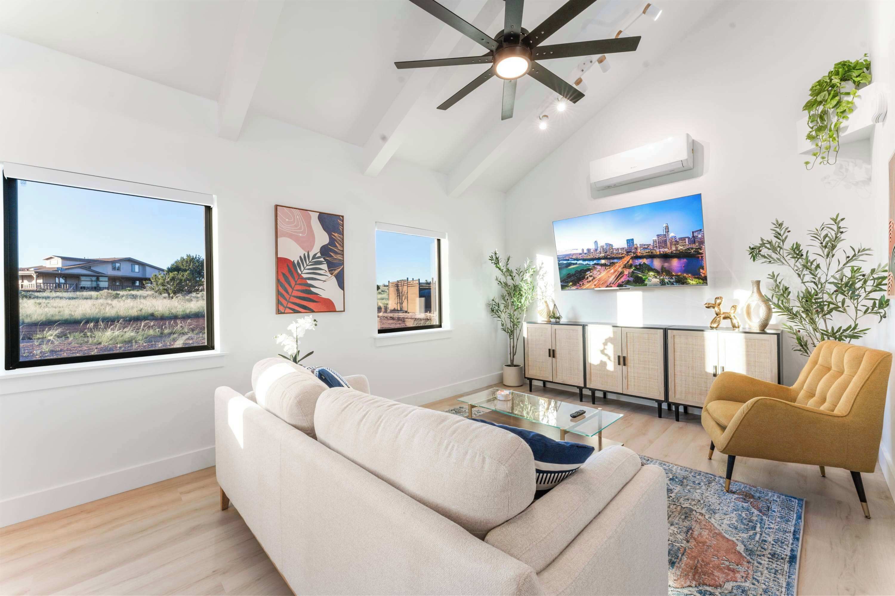 A modern living room with a large window, a ceiling fan, a sofa, a coffee table, a TV, and a cabinet.
