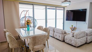 A modern living room with a glass dining table, comfortable seating, a large TV, and a view through large windows. - U-GO Edificio Ocean Drive en Crespo (Cartagena)