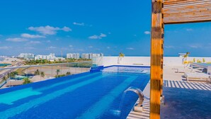 A swimming pool with clear blue water, a wooden pergola, and a view of a cityscape with buildings and palm trees. - U-GO Edificio Ocean Drive en Crespo (Cartagena)