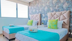 A hotel room with two beds, each with a U-go branded pillow, a blue bedspread, and a white wall with a textured design. - U-GO Edificio Ocean Drive en Crespo (Cartagena)