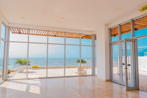 A spacious room with large glass doors leading to a balcony with a view of the sea.