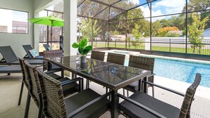 An outdoor patio with a glass table and wicker chairs, overlooking a swimming pool.