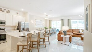 A modern kitchen with white cabinetry, a central island with bar stools, and a dining area with a table and chairs.