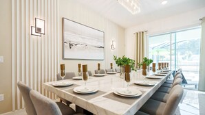 A modern dining room with a long table set for six, featuring a marble top, cushioned chairs, and a large abstract painting above.