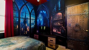 A bedroom with a large bed, a wardrobe, and a shelf with bottles.