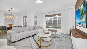 A modern living room with a white sofa, a round coffee table, and a large window with a view of a pool. - Last Minute Disney! Private Pool, Hot Tub, Game Room & Themed Bedrooms. Book Now! #108421 (Orlando)