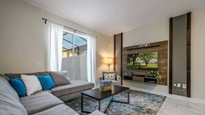 A modern living room with a grey sofa, a coffee table, and a TV mounted on the wall. - Last Minute Disney! Townhouse with Private Pool. Book Now! #CG3435 (Orlando)